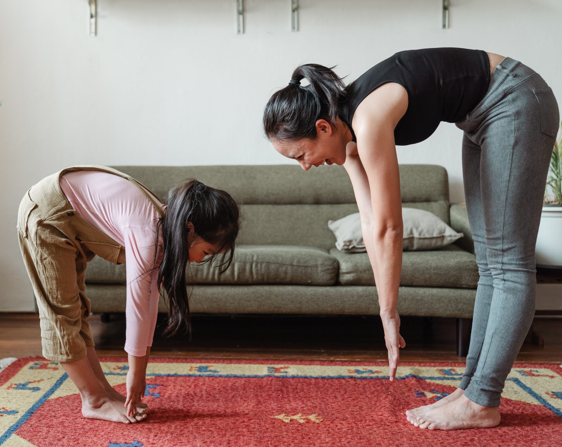 Woman and child face each other while bending over in a stretch and laughing