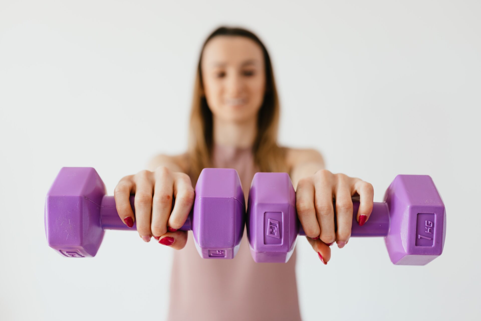 girl holds up two purple dumbbells in front of her