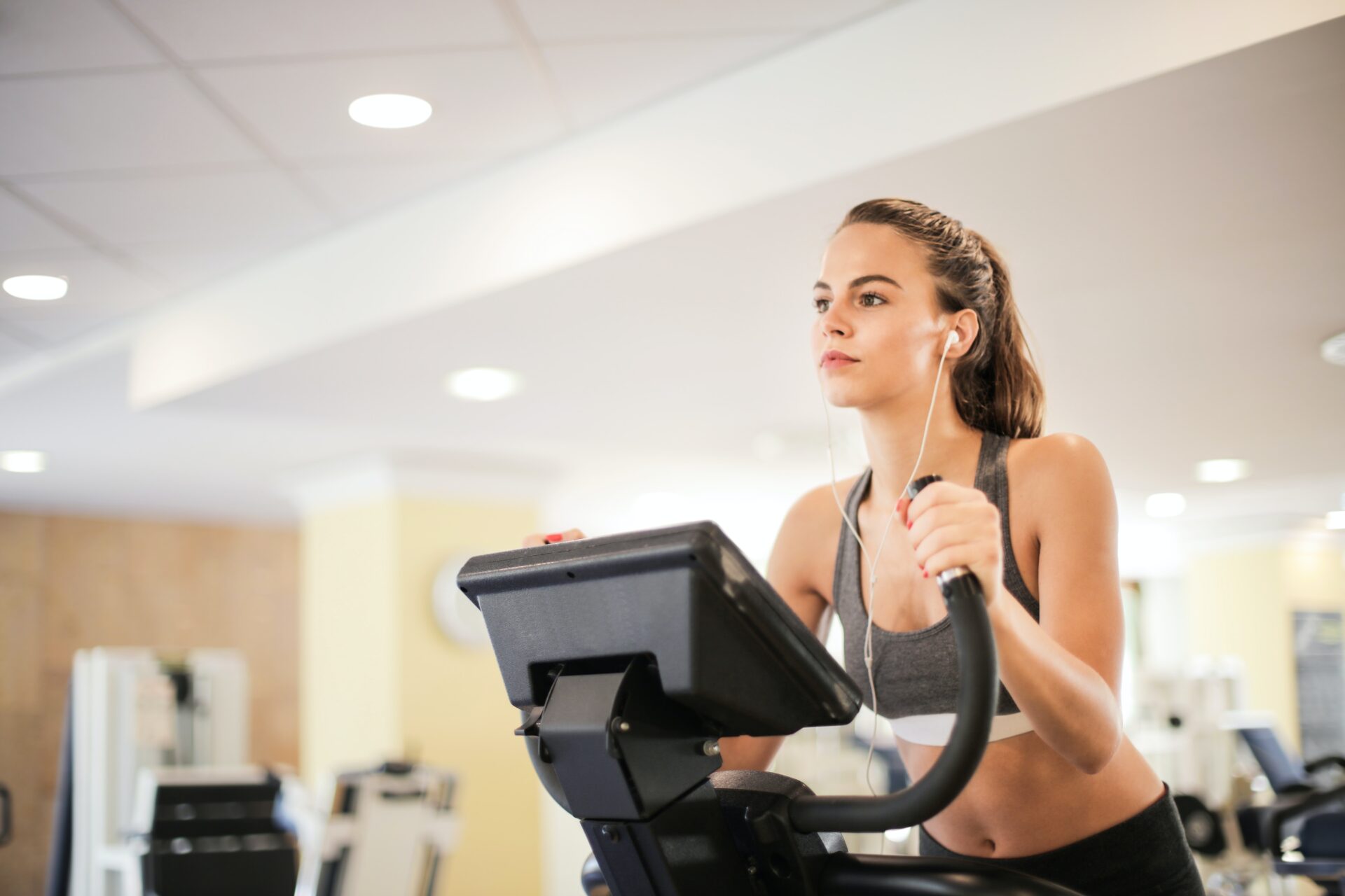 girl wears grey workout clothes with headphones in on the elliptical